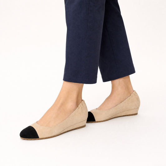 Woman standing in Journey Sand beige suede cap-toe flats with cropped navy trousers, worn on foot