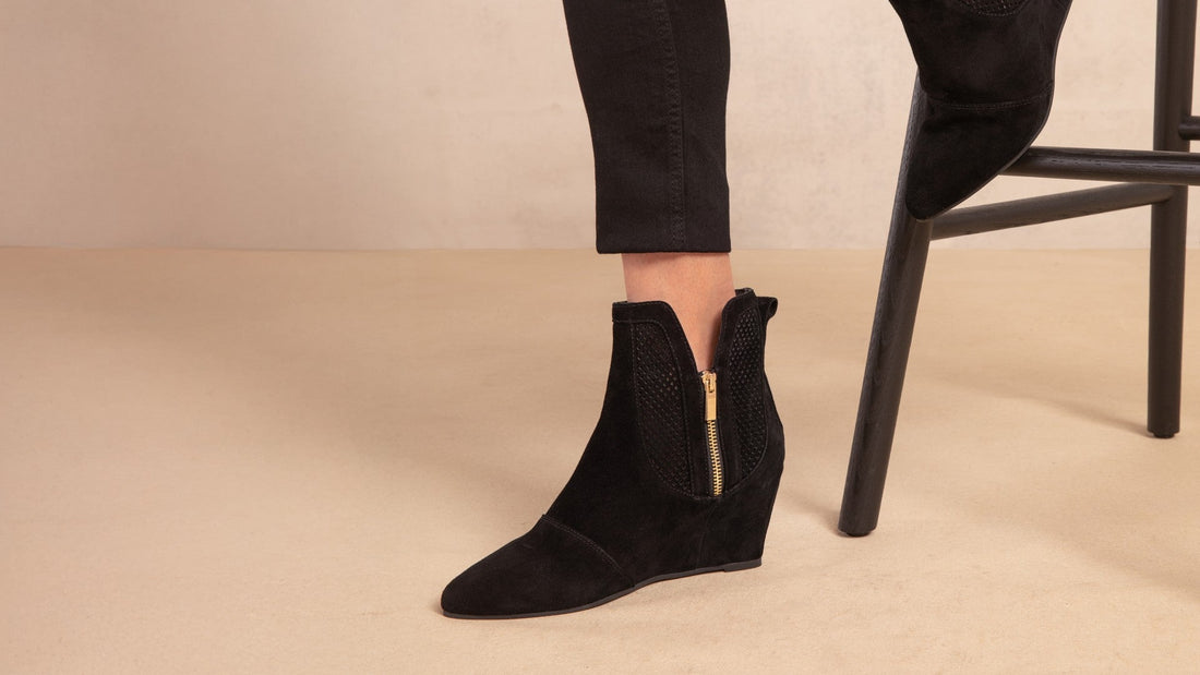 Explorer Space black suede wedge ankle boots worn with black jeans, one foot on a bar stool
