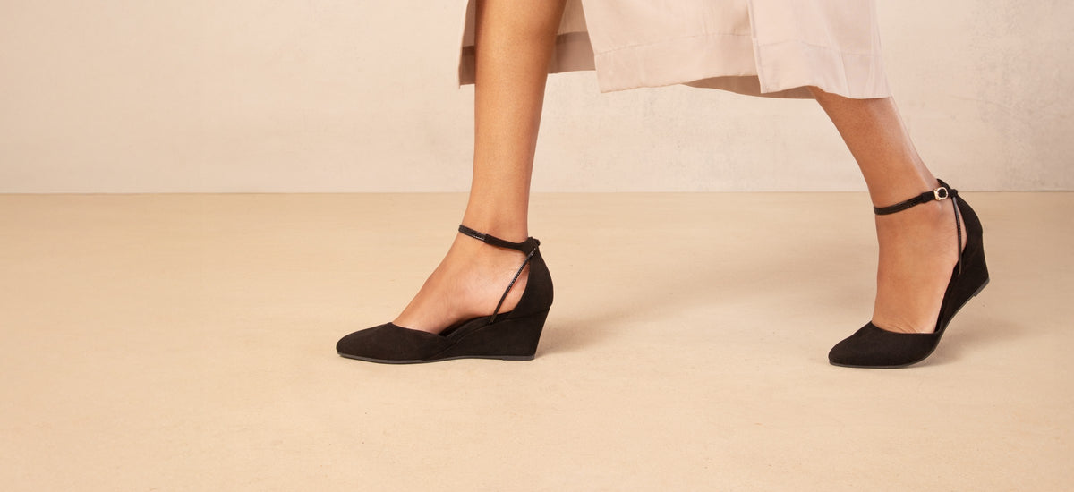 A woman walking in black suede Landmark Space wedges across a cream studio floor